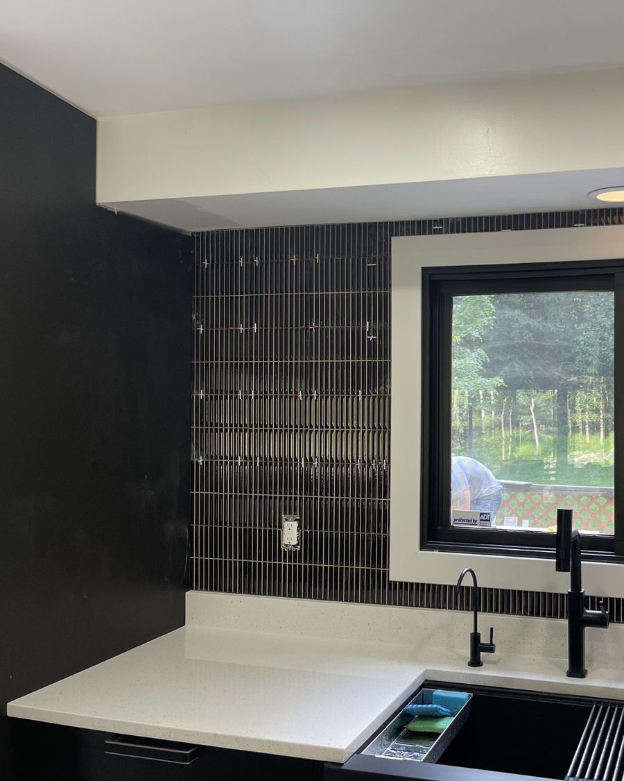 Kitchen window with new white trim and a dark vertical tile backsplash.